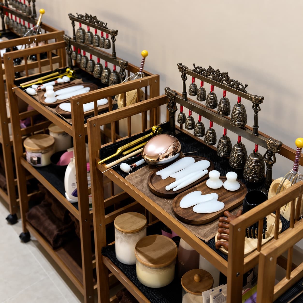 Head spa trolleys set with brass bells, a copper bowl, white stone tools and jars of product